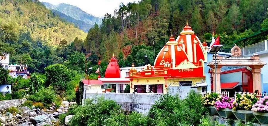 Red-domed temple buildings beside a stream among forested hills at Kainchi Dham