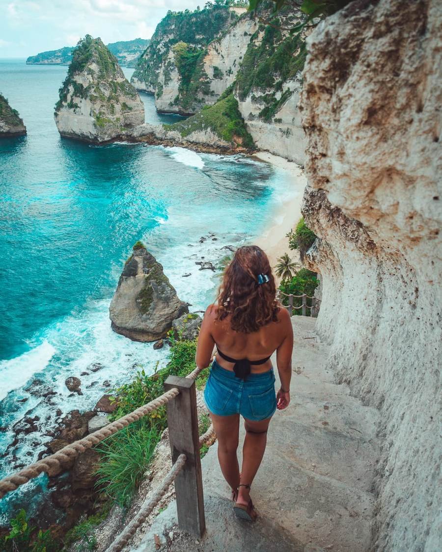 Steps along a limestone cliff above turquoise water and sea stacks on Nusa Penida